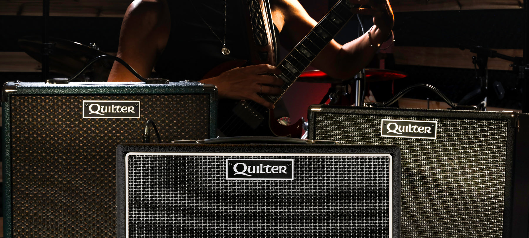 Three Quilter Labs amplifiers with female guitarist standing behind them